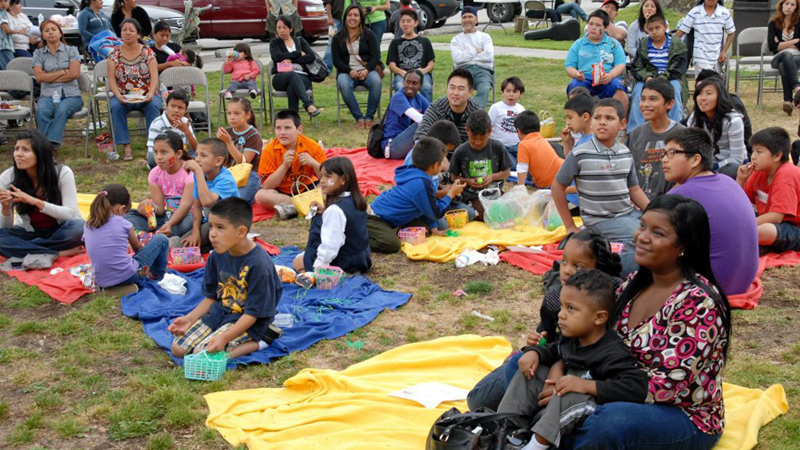 Families sitting on grass looking at subject