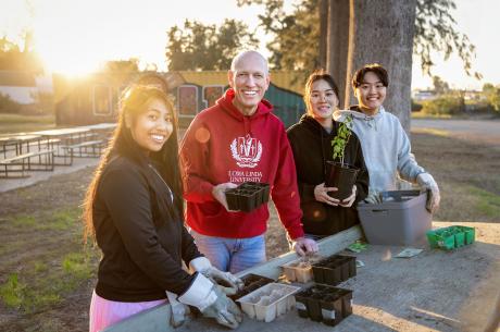 four individuals smiling, gardening at a table outside in hoodie sweatshirts